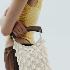 A Zara model wearing a yellow top, brown pants, and carrying a shell bag.