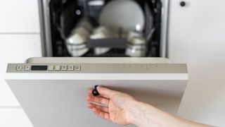 person holding open dishwasher door open to correct a common dishwasher mistake