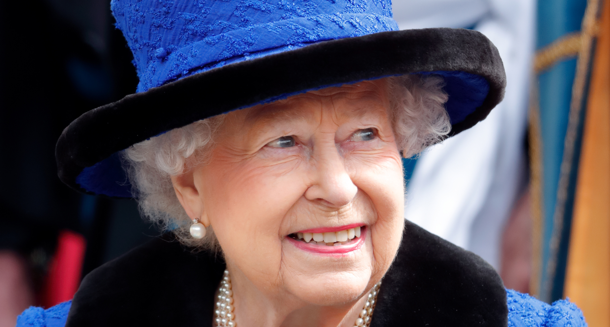 Queen Elizabeth in a bright blue hat smiling