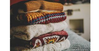 folded winter jumpers on a bed in a bedroom
