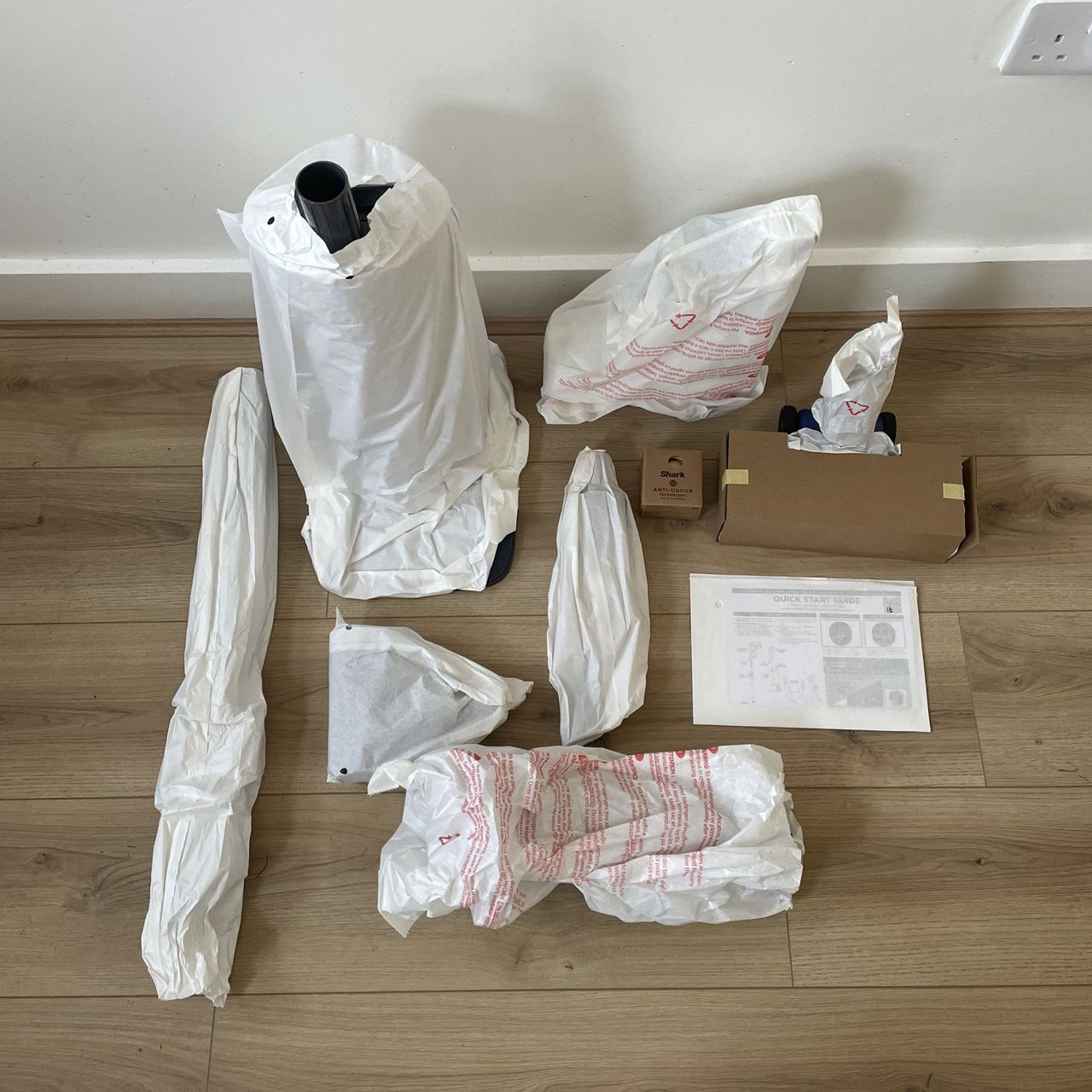 Components of the Shark PowerDetect Speed wrapped in paper and laying on wood-effect flooring