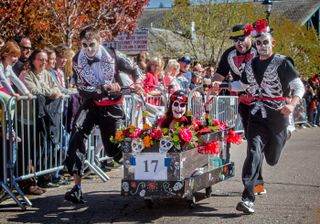 People in Day of the Dead outfits run down a hill with a coffin