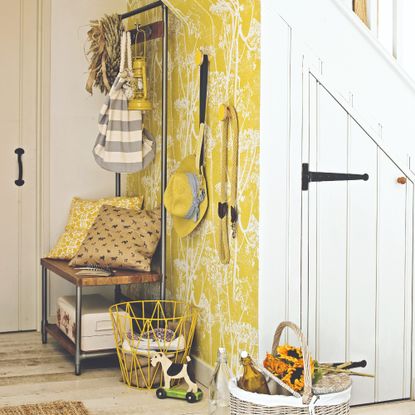 A hallway with a wall covered in a botanical yellow wallpaper and an under stairs storage unit with white doors