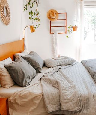 A wooden bed with gray and white bedding and plants on the wall