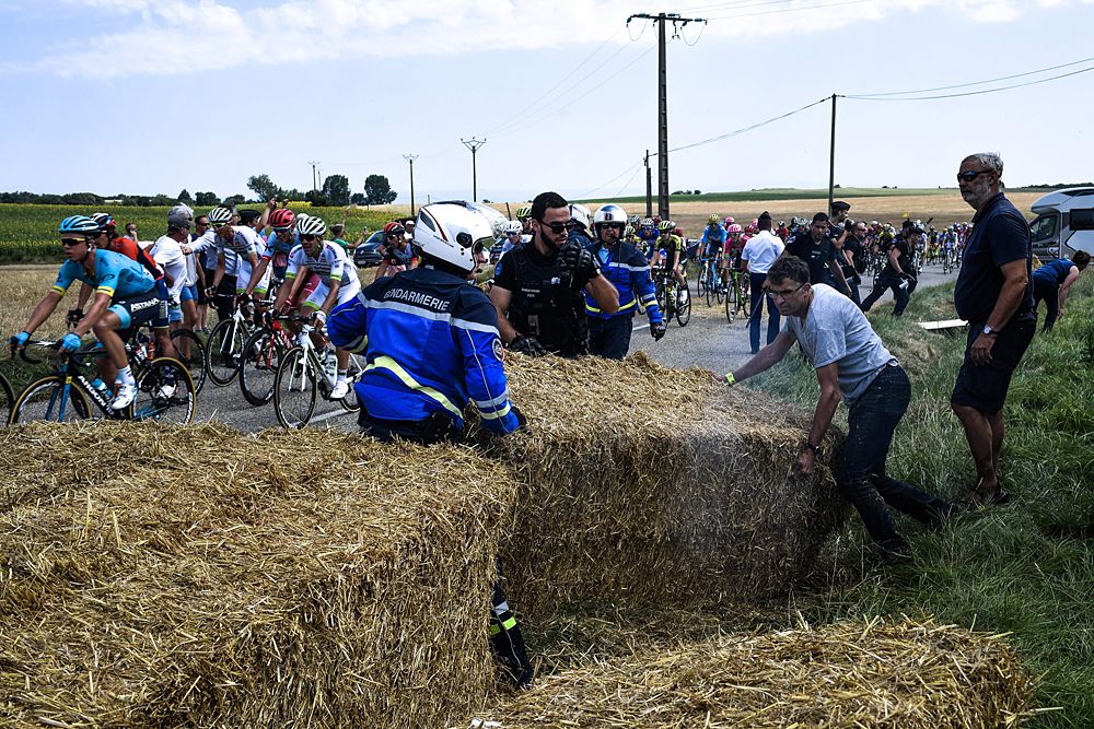Gendarmes (L and R) hold back protesters with a flock of sheep, during a farmers' protest who attempted to block the stage's route with haystacks and sheep