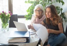 Senior woman and her daughter going through paperwork, using laptop computer