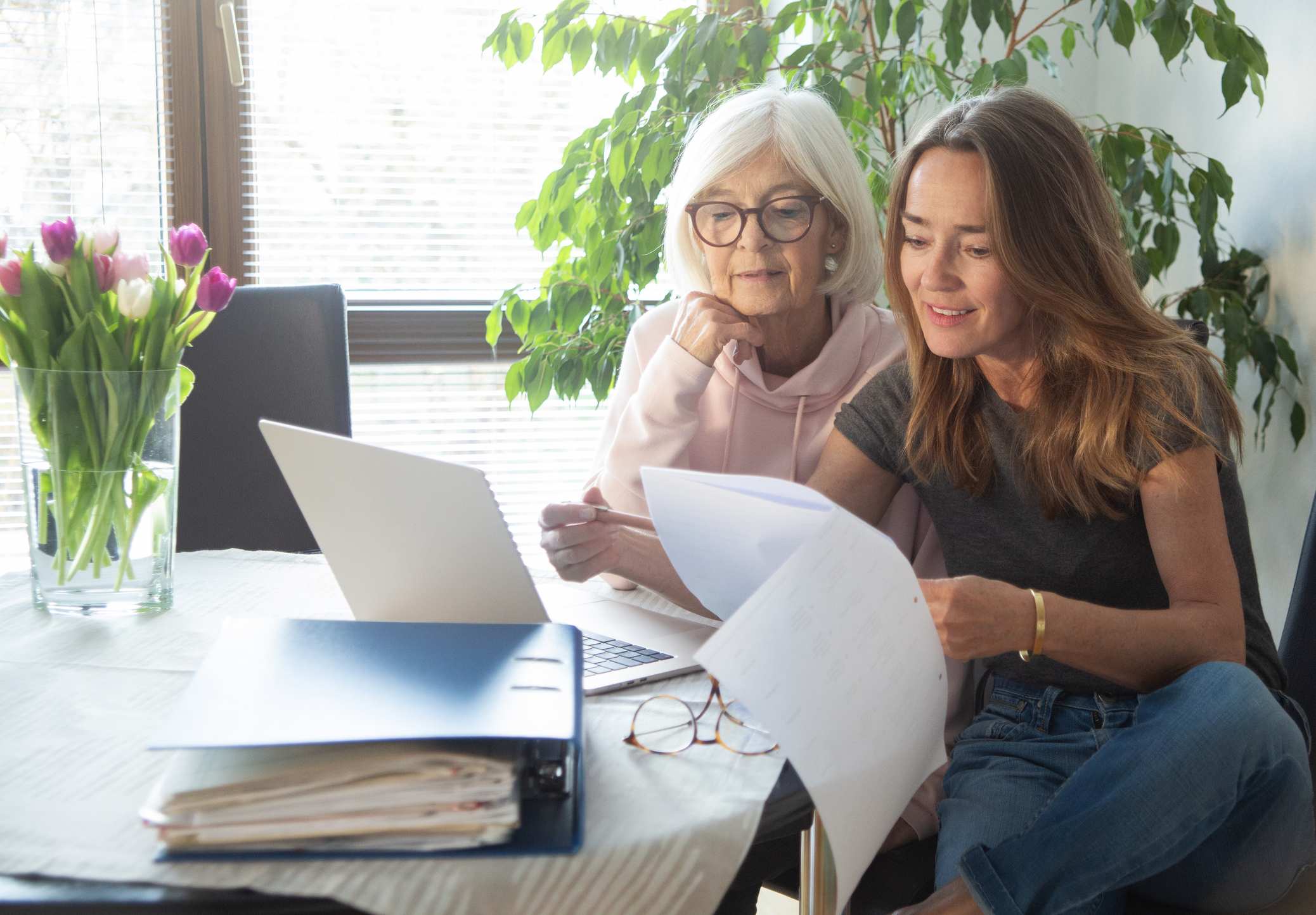 Senior woman and her daughter going through paperwork, using laptop computer
