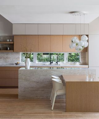 Modern wooden slab kitchen with large island, bar stools and foliage for display