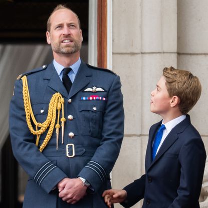 Prince William wearing a blue military coat looking up and standing next to Prince George 