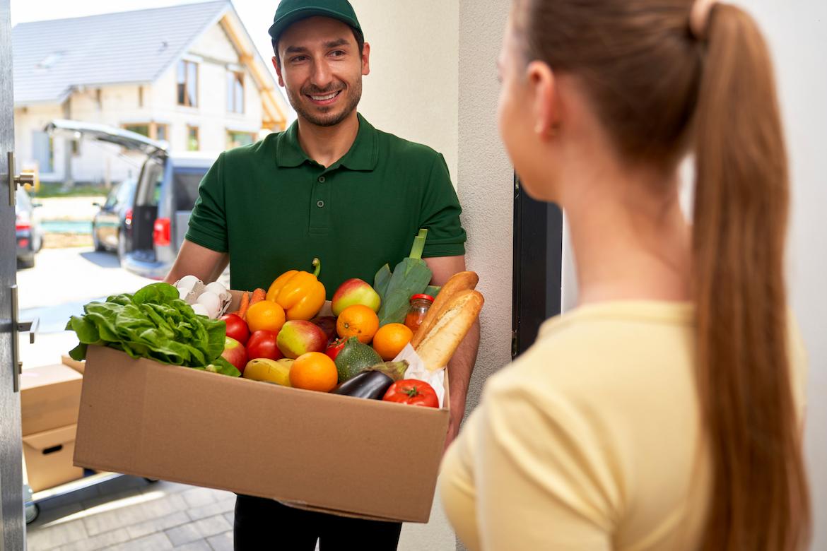 A smiling delivery man handing a woman her groceries at her front door