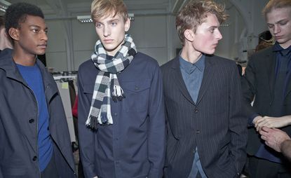 Four men in a line who look part of a fashion show, wearing blazers and coats