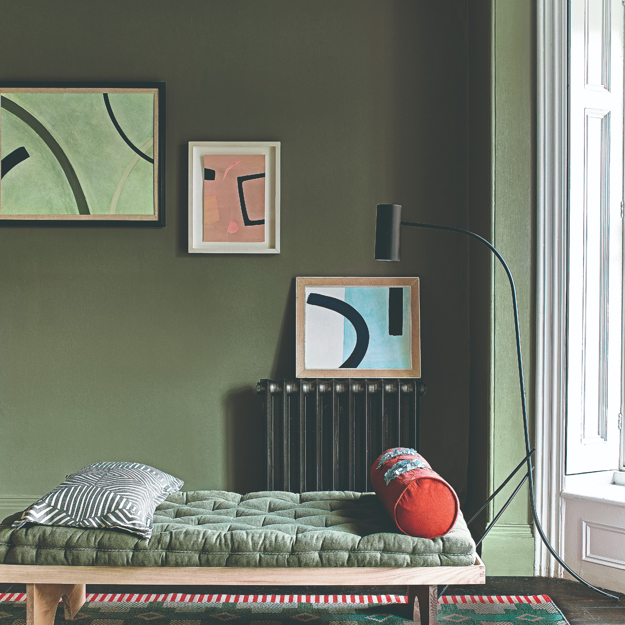 A green living room with abstract painting on the wall and a day bed