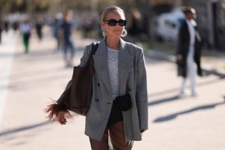 a guest wear chunky hoop earrings, sunglasses, and a grey blazer at fashion week