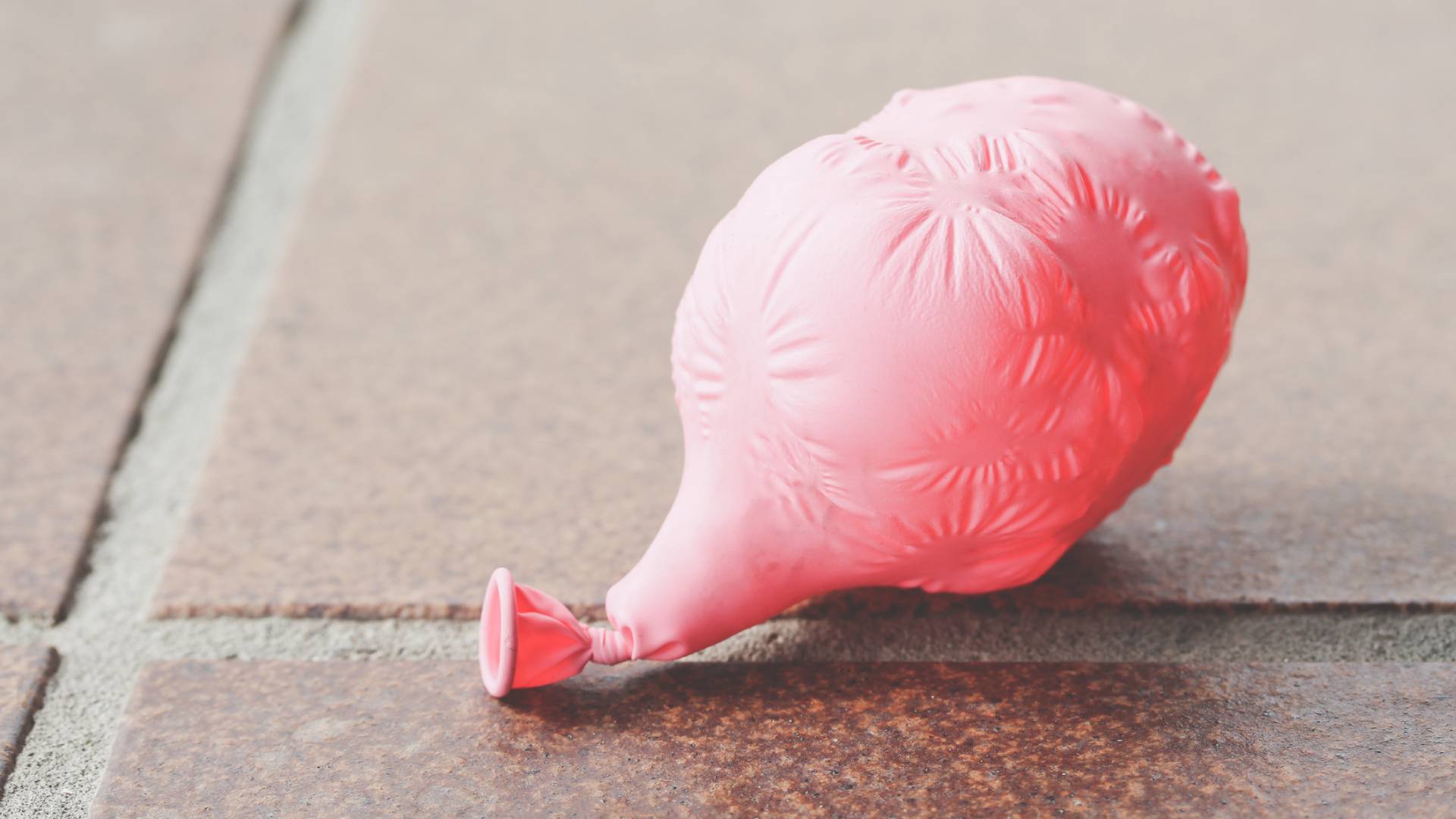 A pink balloon deflated lying on a tiled floor.