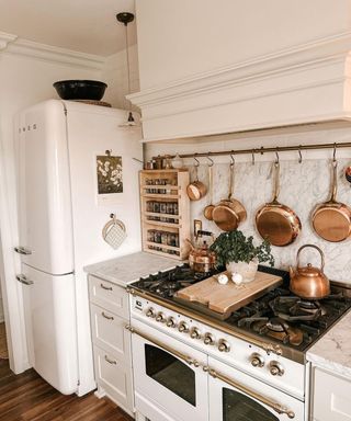 A white kitchen with a stove, fridge, and copper pans and a kettle