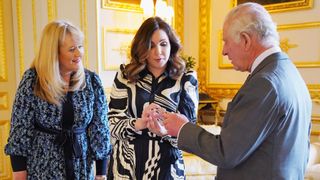 WINDSOR, ENGLAND - APRIL 13: King Charles III is presented with the first struck £5 Coronation coin by Royal Mint CEO Anne Jessopp (left) and Director Rebecca Morgan (centre) on April 13, 2023 at Windsor Castle, Windsor, England. A crowned portrait of the King will for the first time feature on a new range of commemorative coins created to celebrate the upcoming coronation. The collection, which includes a 50p and £5 coin, will be released later this month ahead of the historic May 6 celebration.