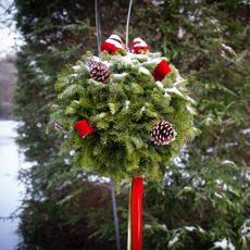 Evergreen kissing ball with red accents outside in snow