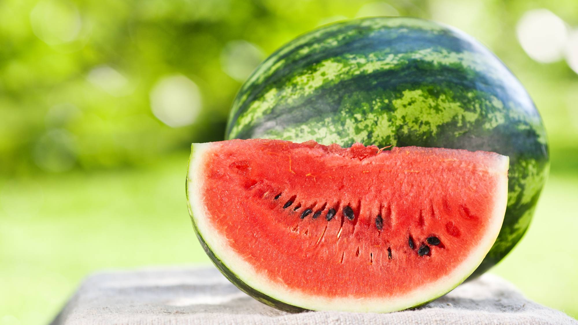 A slice of watermelon and a whole watermelon outdoors