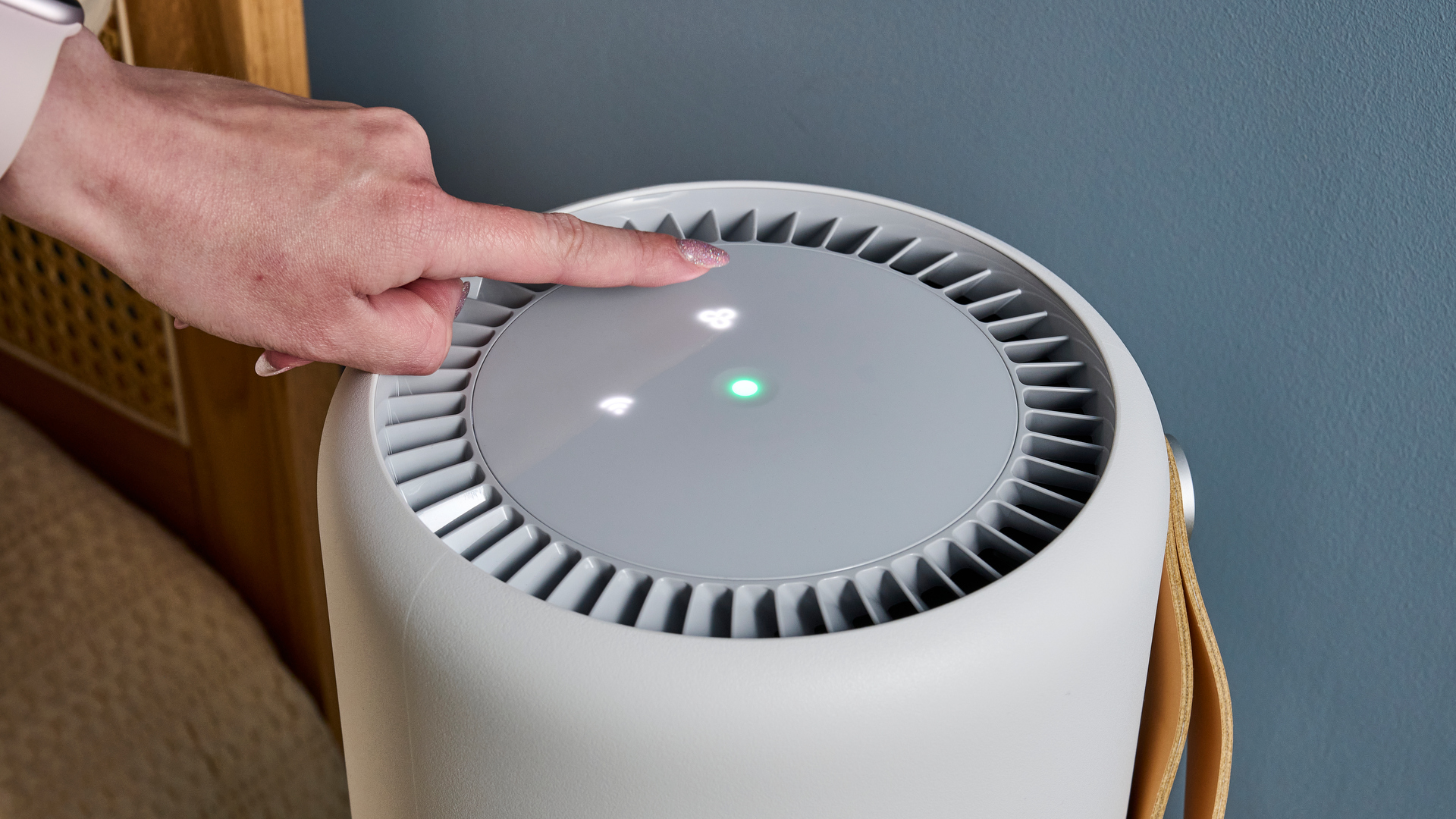 Picture shows a the top of the Molekule Air Mini Plus air purifier, with a finger nearly pressing the illuminated auto protect button.