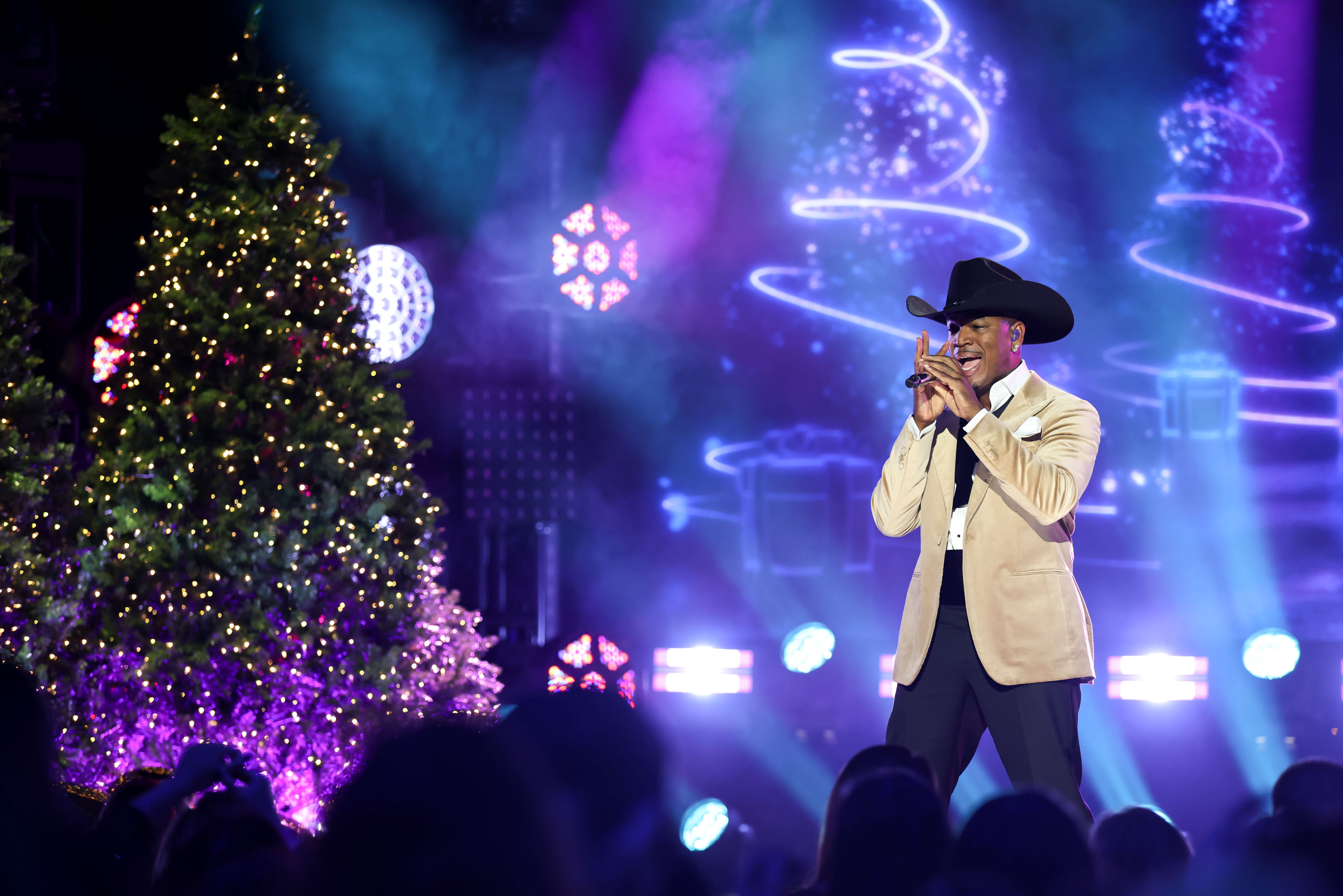 ne-yo wears a white suit and cowboy hat while singing on stage next to a christmas tree during nbc&#039;s christmas in nashville special