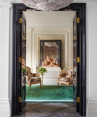 Hall with terracotta sculpture, plaster chandelier, green rug and gilded, patterned chairs in Edwardian house in West London designed by Philip Vergeylen of Nicholas Haslam