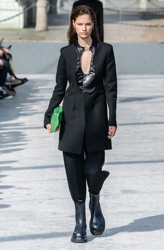 Woman wears black cut out tuxedo with stomper boots and a green bag