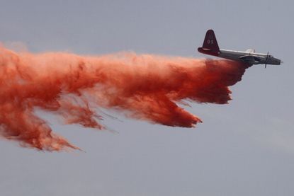 A firefighting air tanker drops retardant on a fire.