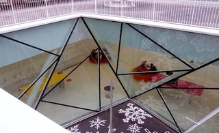 View into underground space looking through glass ceiling constructed of triangular panes of glass with black trims.