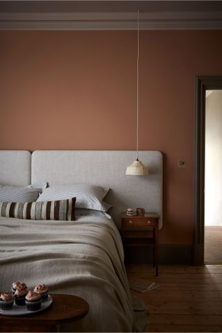 Terracotta bedroom with linen soft headboard and bedding, low pendant light above wood beside table