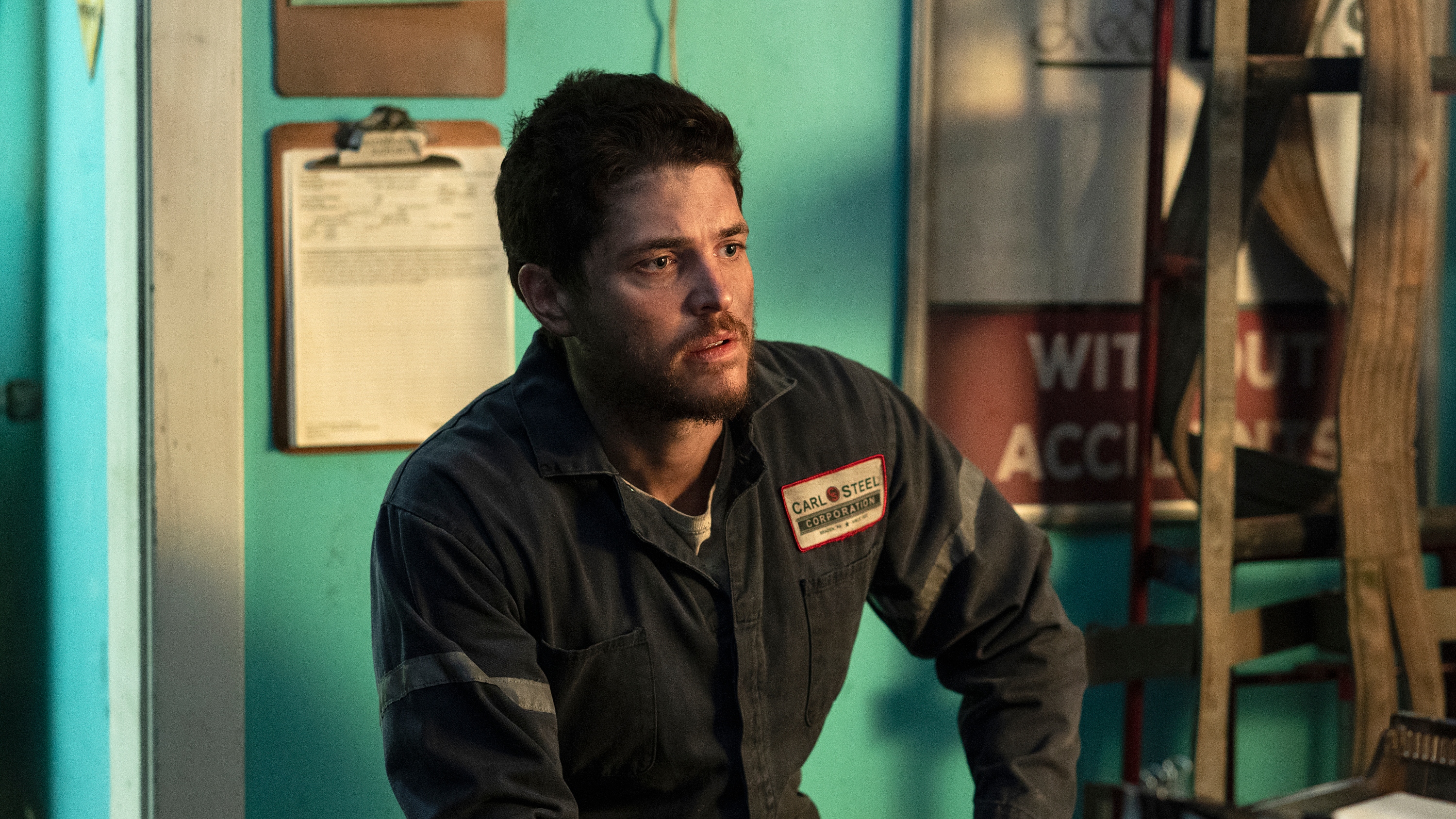 Philip Ettinger as Garrett Drimmer wearing overalls with the words 'Carl Steel Corporation' on the badge.