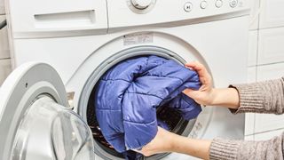 blue puffer coat being put into a washing machine