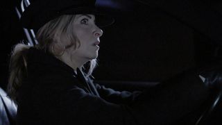 Charity wearing a chauffer's hat and driving a limo in the dark