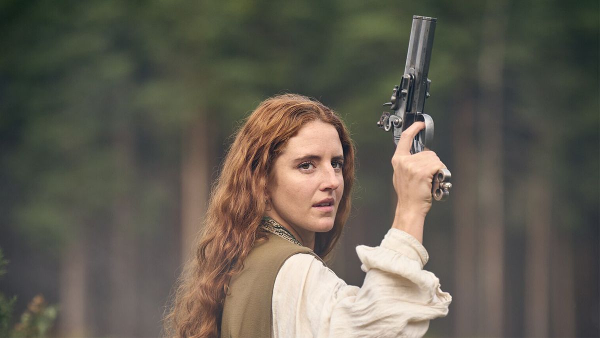 A woman stands holding a gun above her head