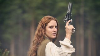 A woman stands holding a gun above her head