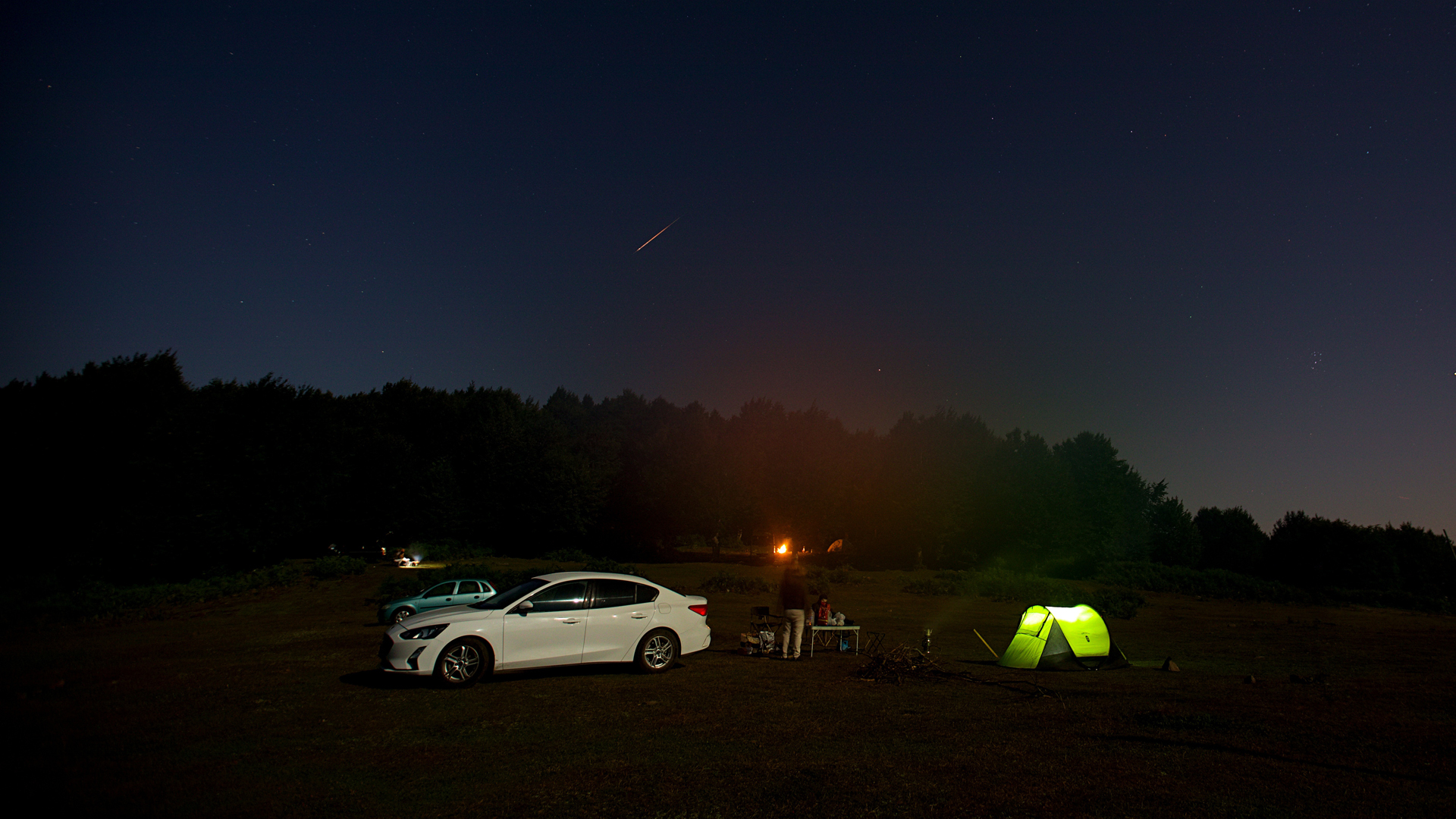 A Perseid meteor streaks over a campsite with a green tent in Turkey