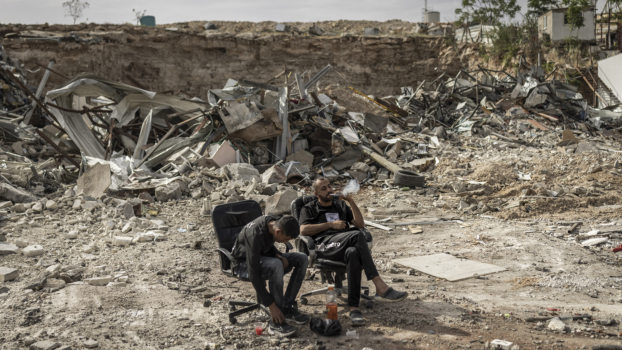 Two Palestinian men relax amongst the ruins of businesses that were demolished by Israeli forces in the Israeli-occupied West Bank town of al-Eizariya