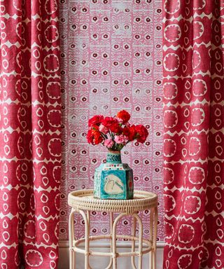 An example of how to hang wallpaper in a red patterned scheme with long red drapes and a wicker side table.