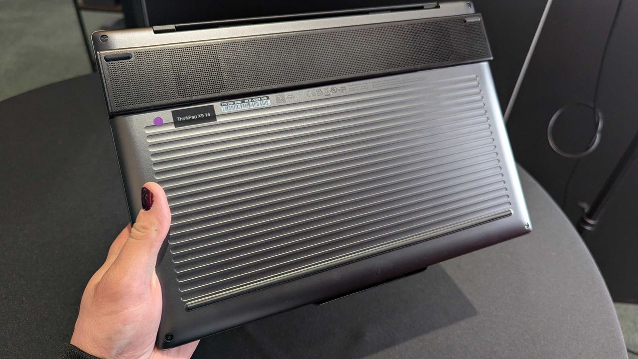 The Lenovo ThinkPad X9 Aura Edition held in the hand, showing its corrugated bottom and "Engine Hub."