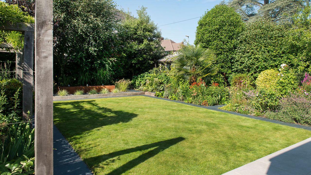 Cut grass lawn in garden surrounded by border plants and trees