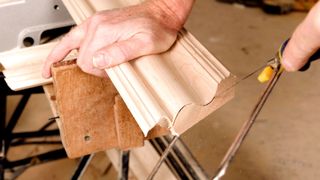 Hand holding skirting board and using a coping saw to scribe the end