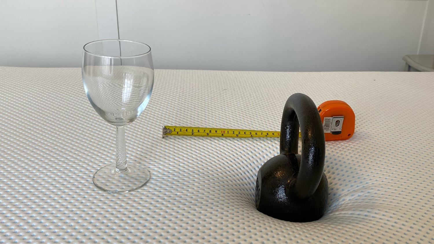 A weight. a wine glass and a tape measure on the Amerisleep AS3 Hybrid mattress