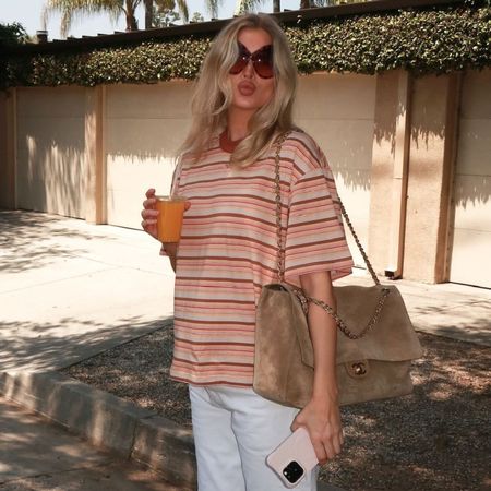 Elsa Hosk holds an orange juice wearing a striped t-shirt with white jeans and brown flip-flops.
