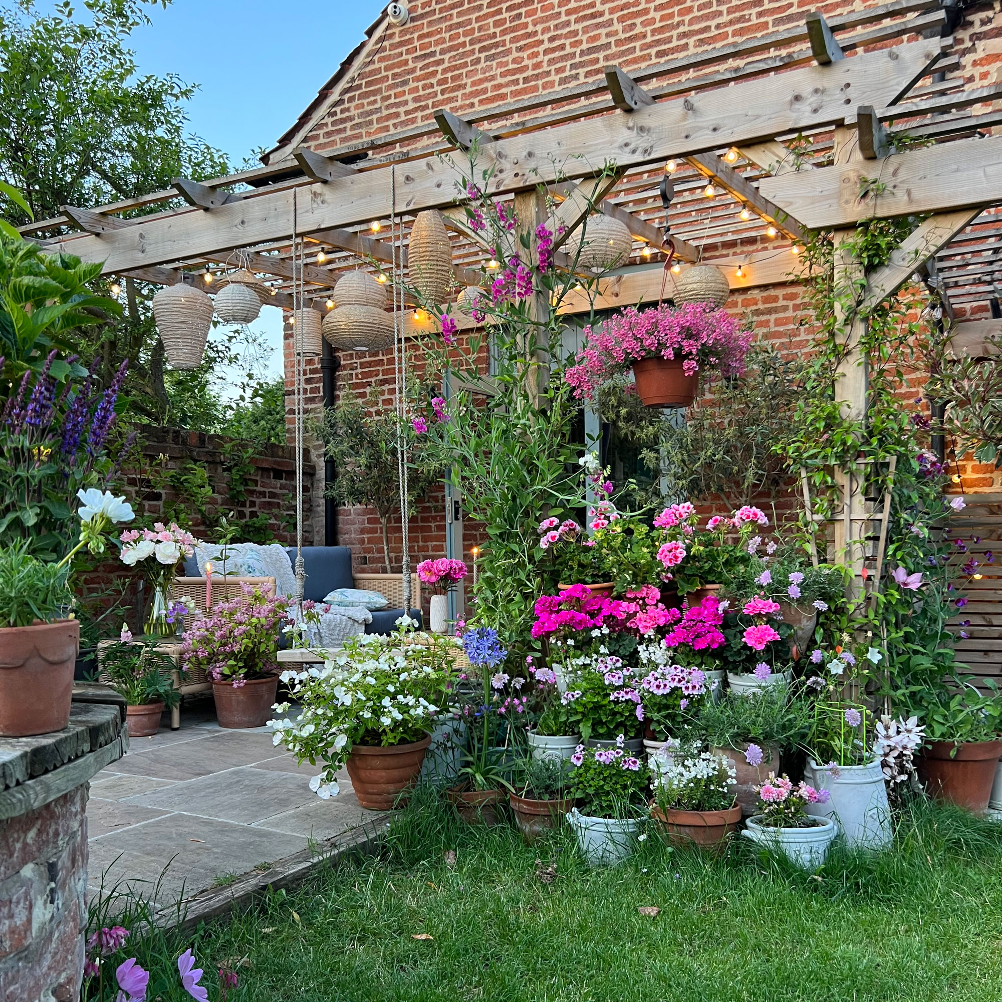 Wooden pergola with plants around it and lanterns