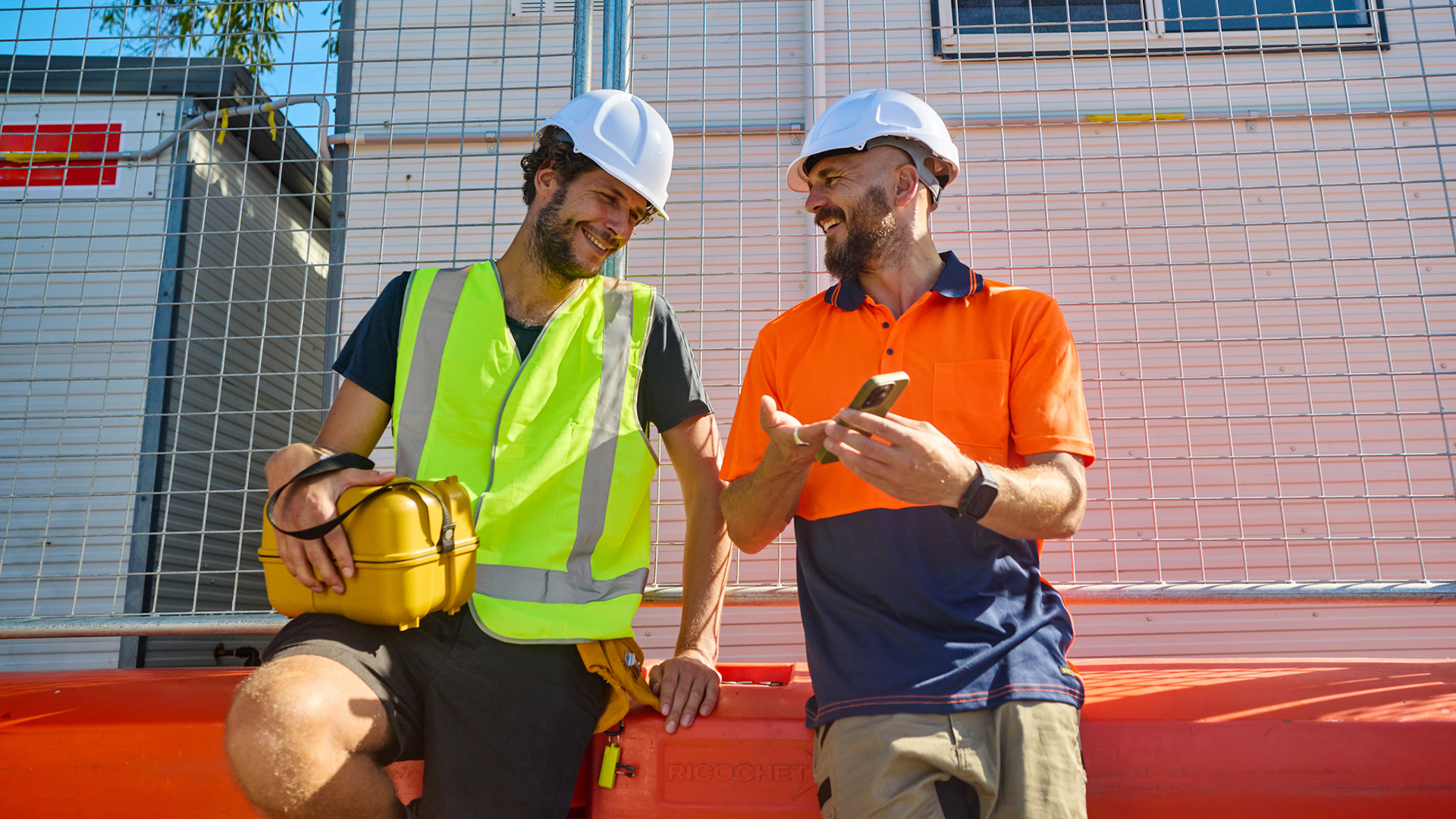 Two tradies in high-vis gear looking at a mobile phone and smiling