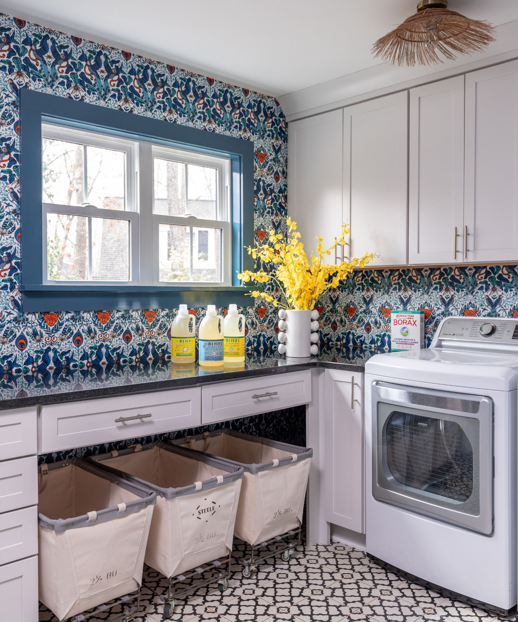 A laundry room decorated with white cabinetry, black and white patterned floor tiles, and a blue and red damask wallpaper