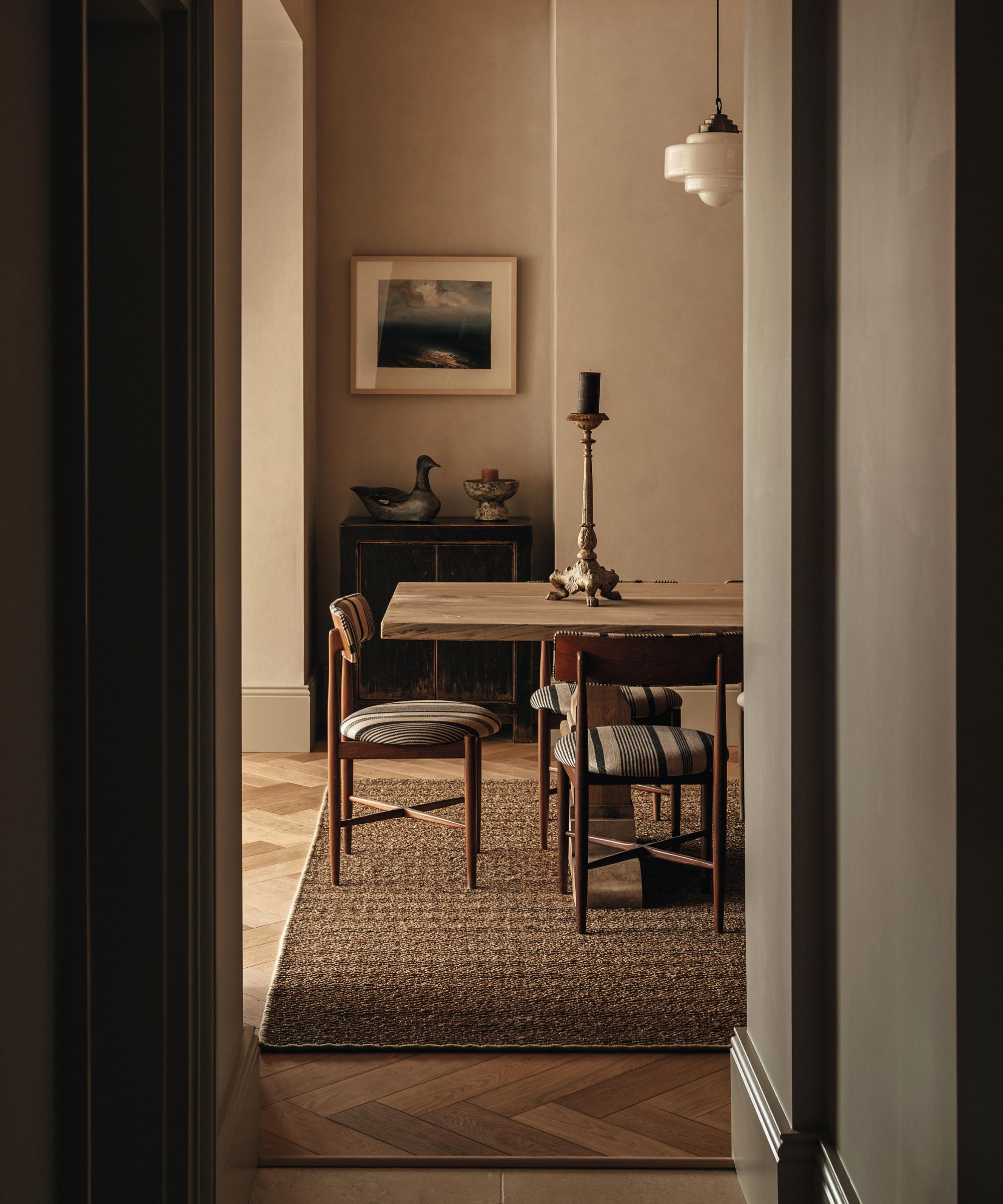 looking through to an earthy dining room with a wooden rustic table and wooden chairs with striped cushions and a woven seagrass rug