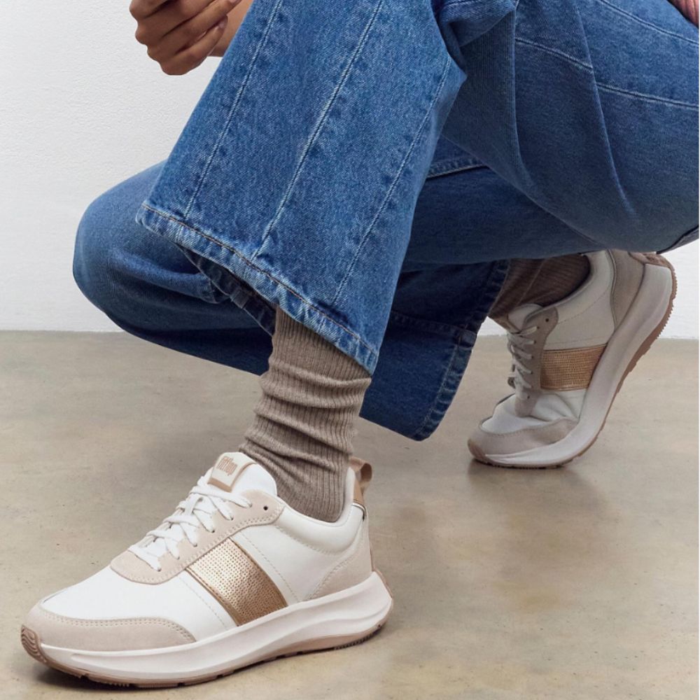 Woman wearing FitFlop white and gold trainers, bending down.