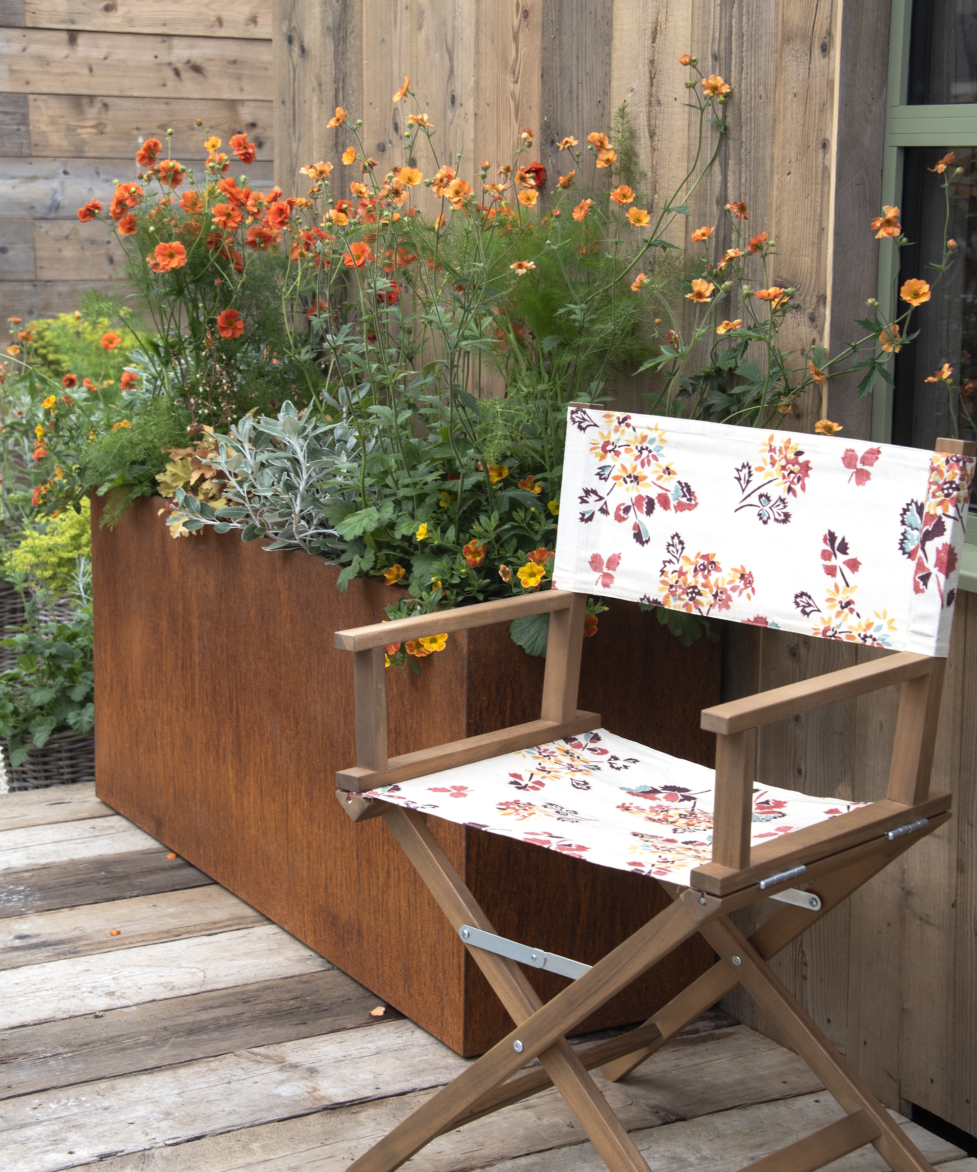 A metal container with bright annual flowers next to a chair with a floral pattern