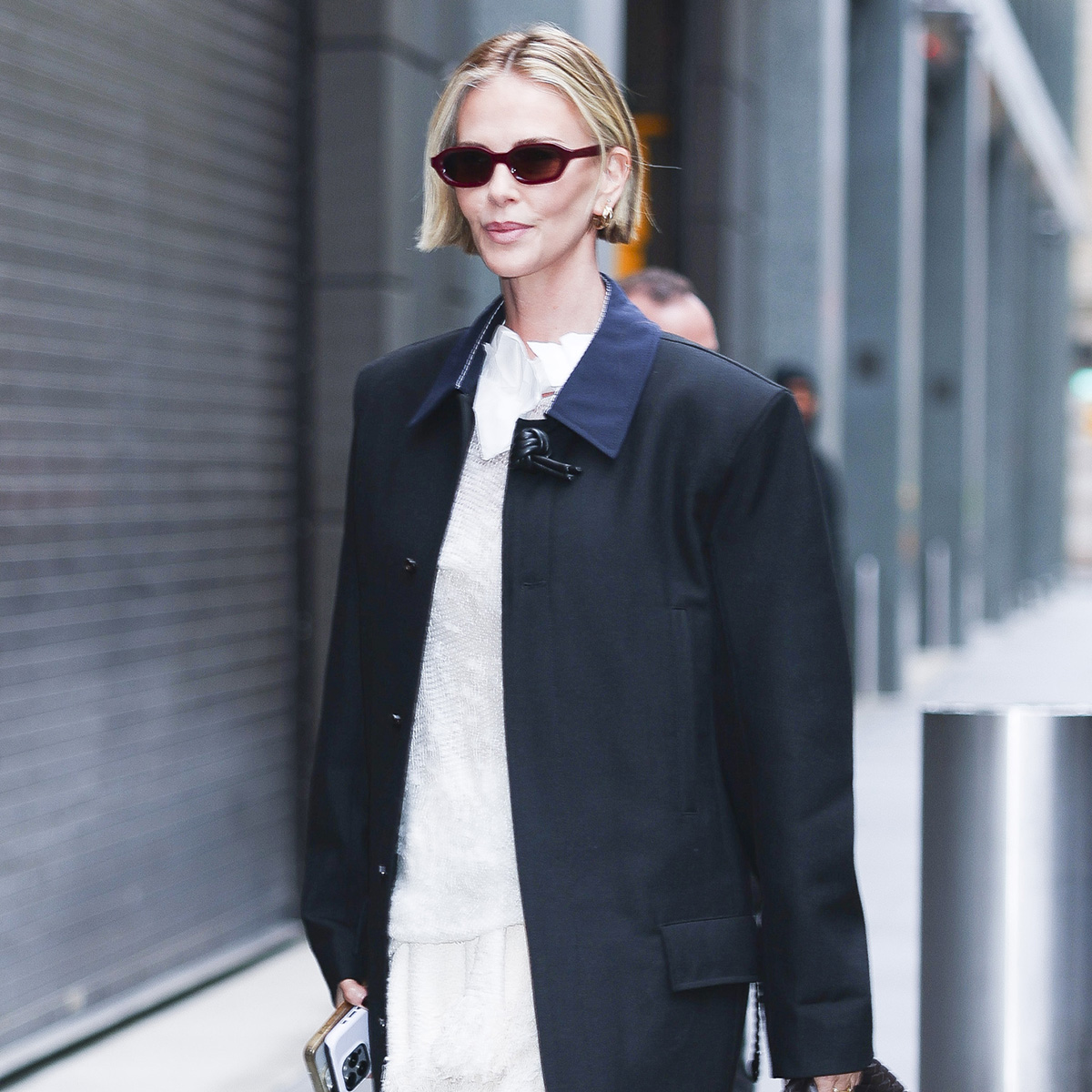 Charlize Theron wearing a black coat over a white top and skirt with soft oxford flats in white leather