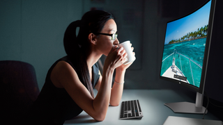 A woman sipping coffee staring at a photograph on a curved monitor